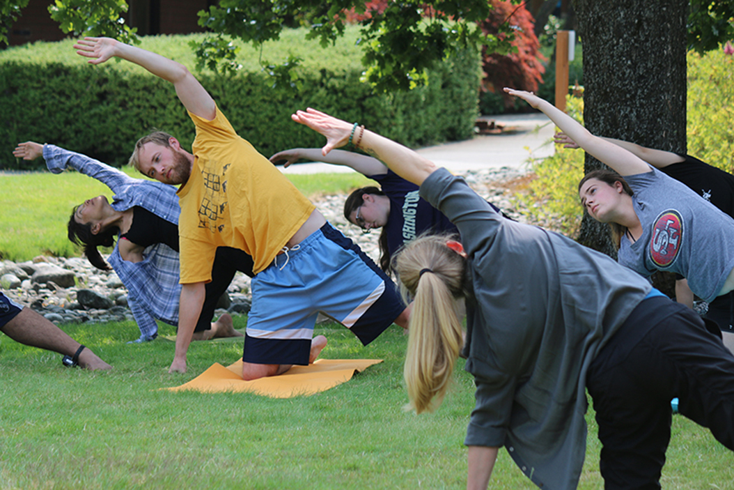 Students follow an instructor doing yoga in a park.